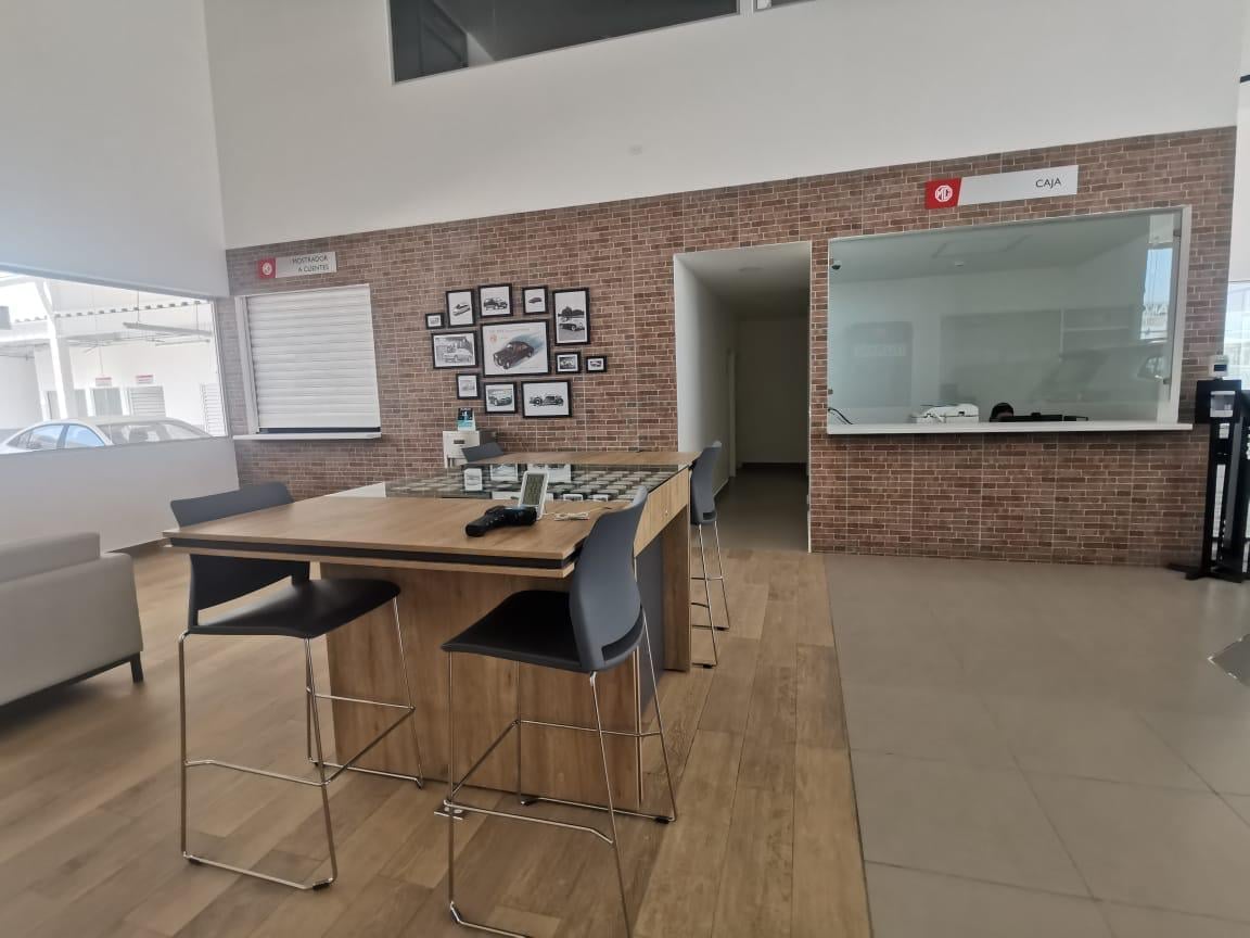 Modern office space with tall wooden table, bar stools, brick wall, glass partition window, and framed artwork displays