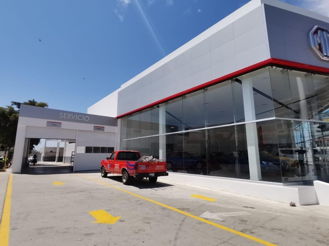 Modern auto service dealership with white and red facade, large windows, and a red vehicle parked in front under clear blue sky